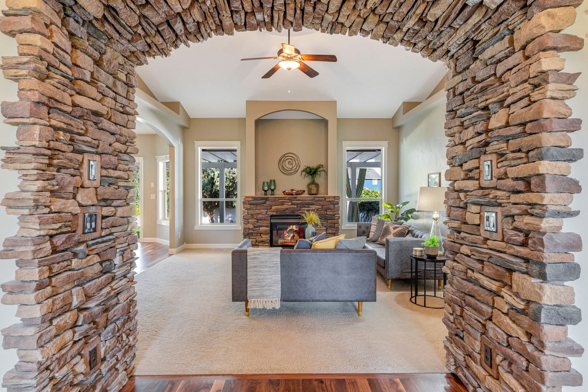 Stacked-stone archway framing a living room with a fireplace and ceiling fan