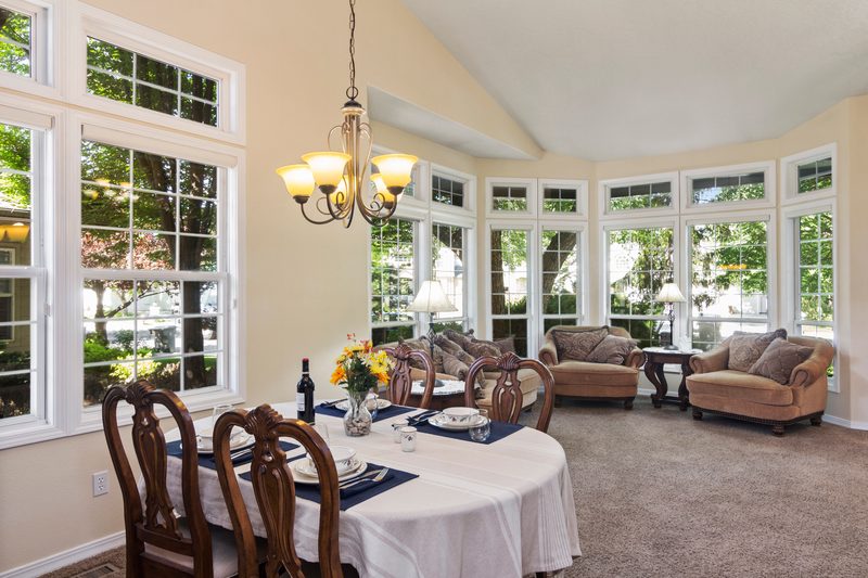 Dining table under a chandelier in a sunny bay-window nook next to a sitting area