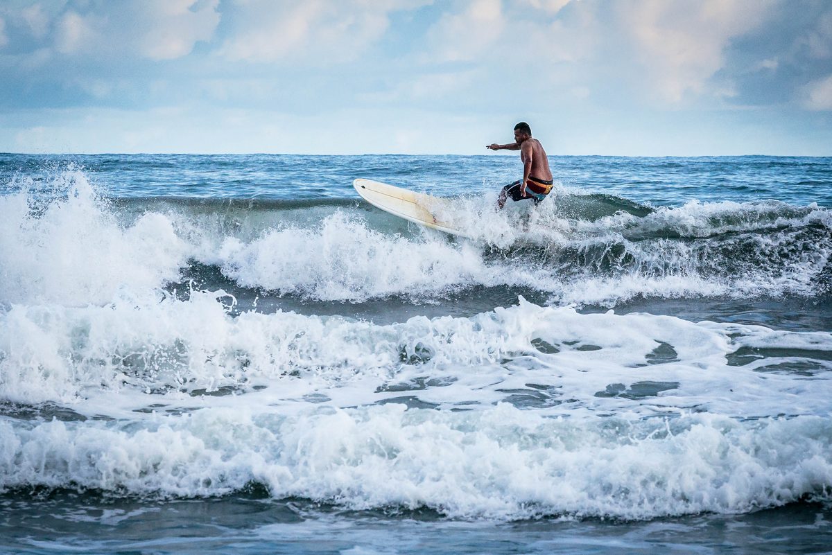 A surfer carving across a breaking wave under a blue sky in Costa Rica
