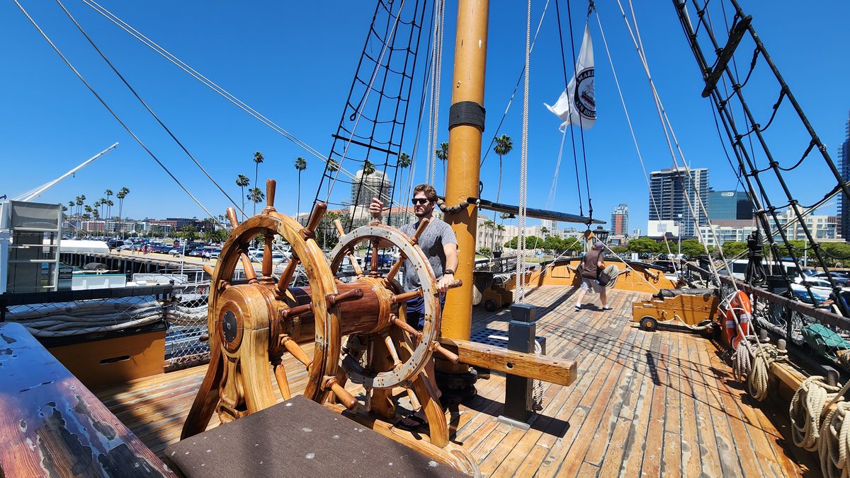 The wooden ship's wheel on the deck of a historic tall ship in harbor