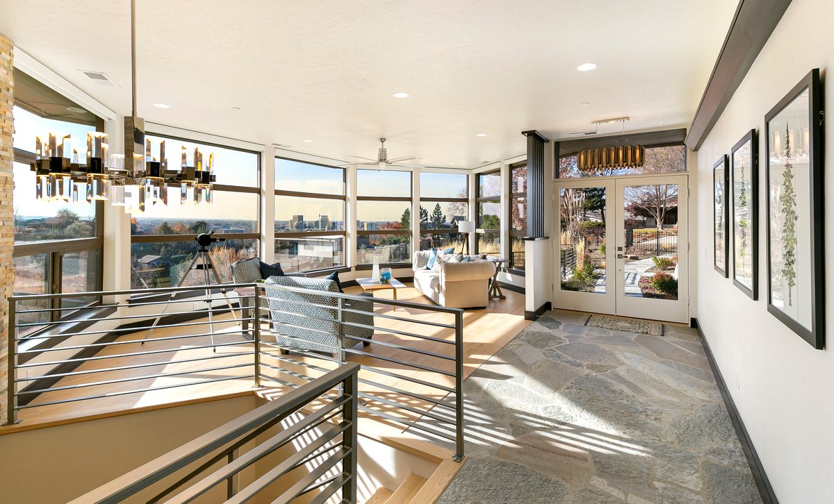 Bright loft hallway with a modern railing, wraparound windows and an open kitchen beyond