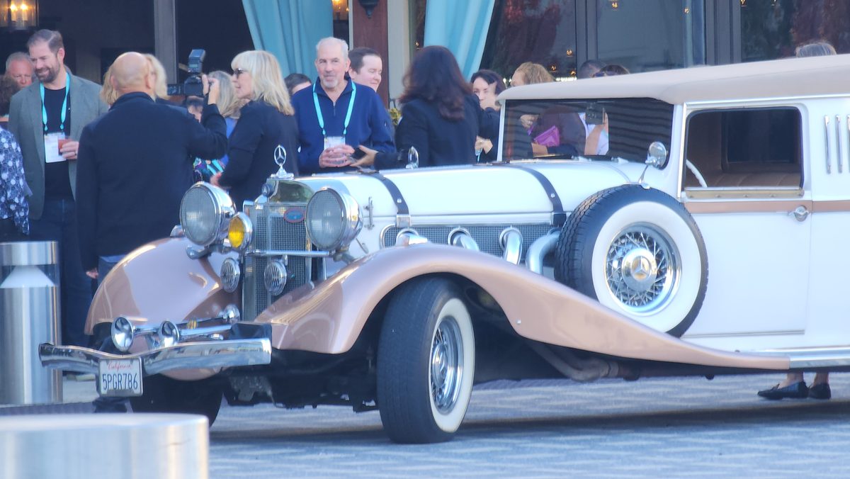 A white and tan vintage roadster with chrome trim at an event