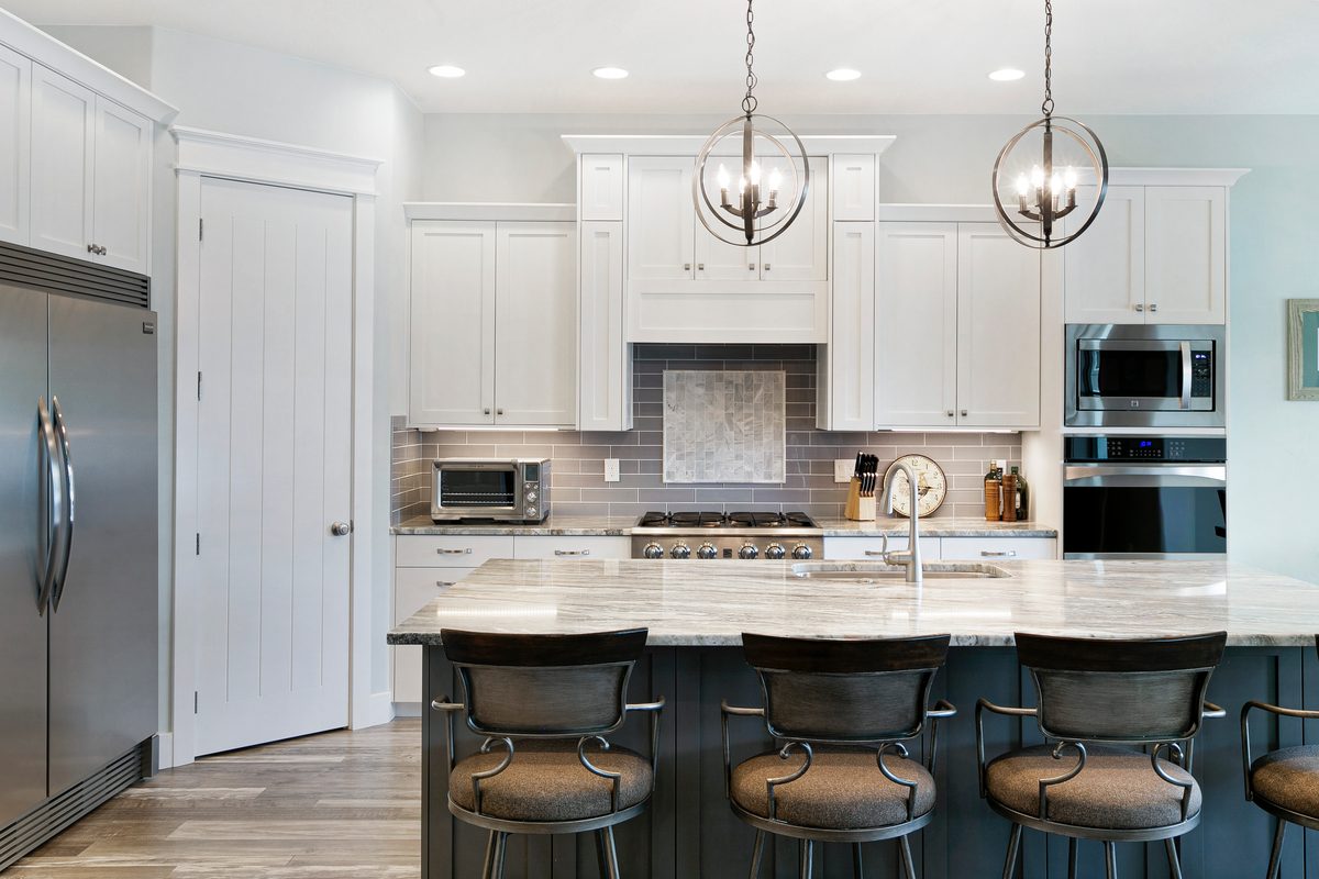 White kitchen with an island, three bar stools, pendant lights and stainless appliances