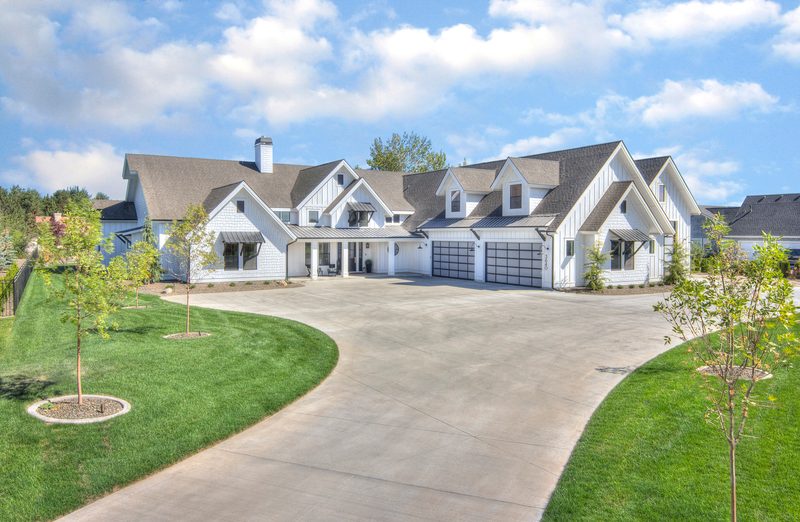 White modern farmhouse with black trim, a big driveway and young trees