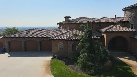 Drone orbits a Tuscan-style hilltop villa with a tile roof and tower